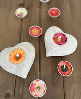 Two white marble heart tea light holders with floral scented tealights on a wooden surface